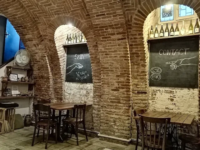 A vaulted brick cellar with chalkboards, wine bottles on the stone ledges and wooden tables