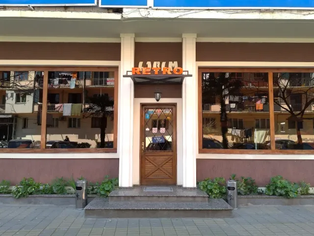 A building facade with a wooden door, two large display windows and shrubs on the pavement