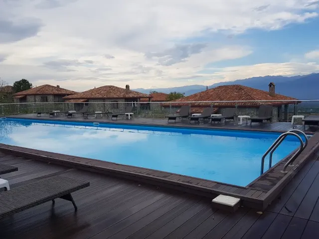 A swimming pool on a wooden deck, stone buildings with tiled roofs and a mountain ridge behind