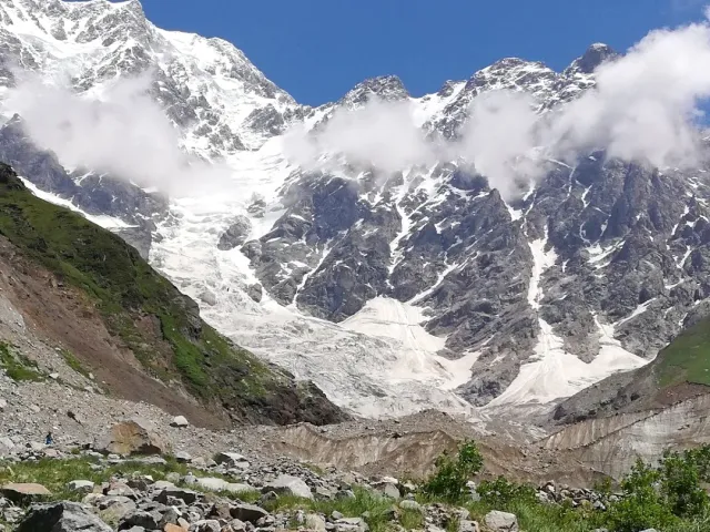 Snow covered peaks wrapped in clouds above a glacier tongue with scattered boulders in front