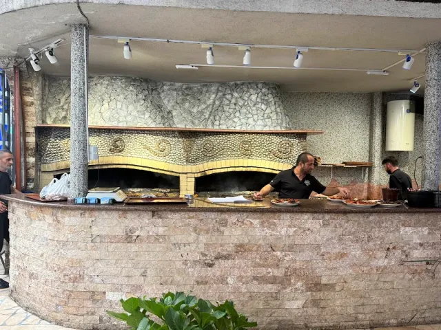 Two cooks working behind a stone counter at an open charcoal grill, under spotlights