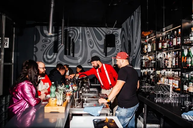 Bartenders mixing drinks for guests at a dark counter with shelves of bottles