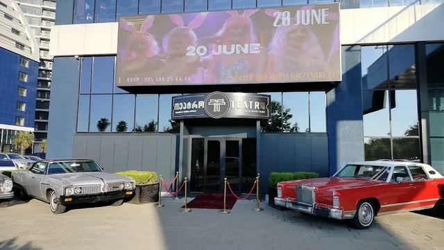 An entrance with a red carpet and rope barriers, with two classic cars parked beside it