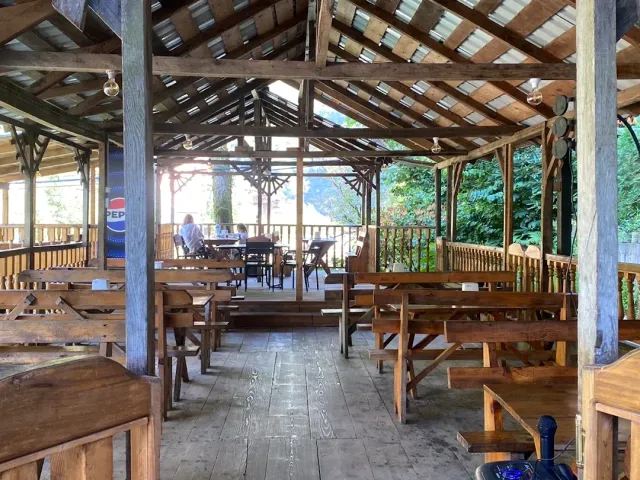 An open wooden pavilion with benches and tables under a metal roof, and green trees around
