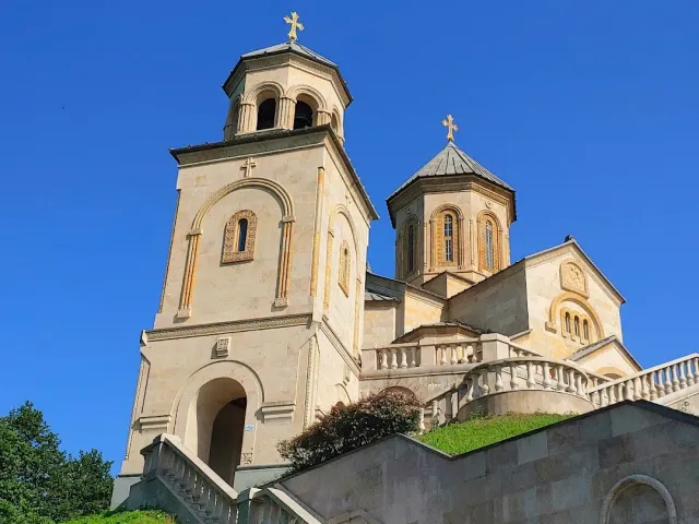 A pale stone church with a bell tower and a dome, above a staircase under blue skies