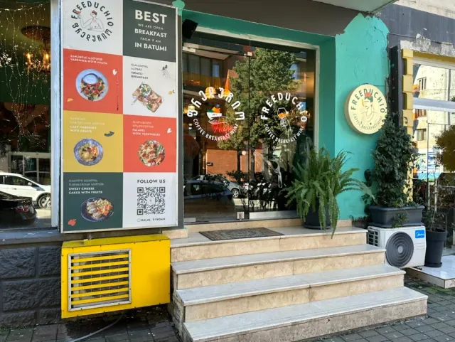 An illustrated menu board beside a turquoise facade with stone steps, potted plants and a shop window
