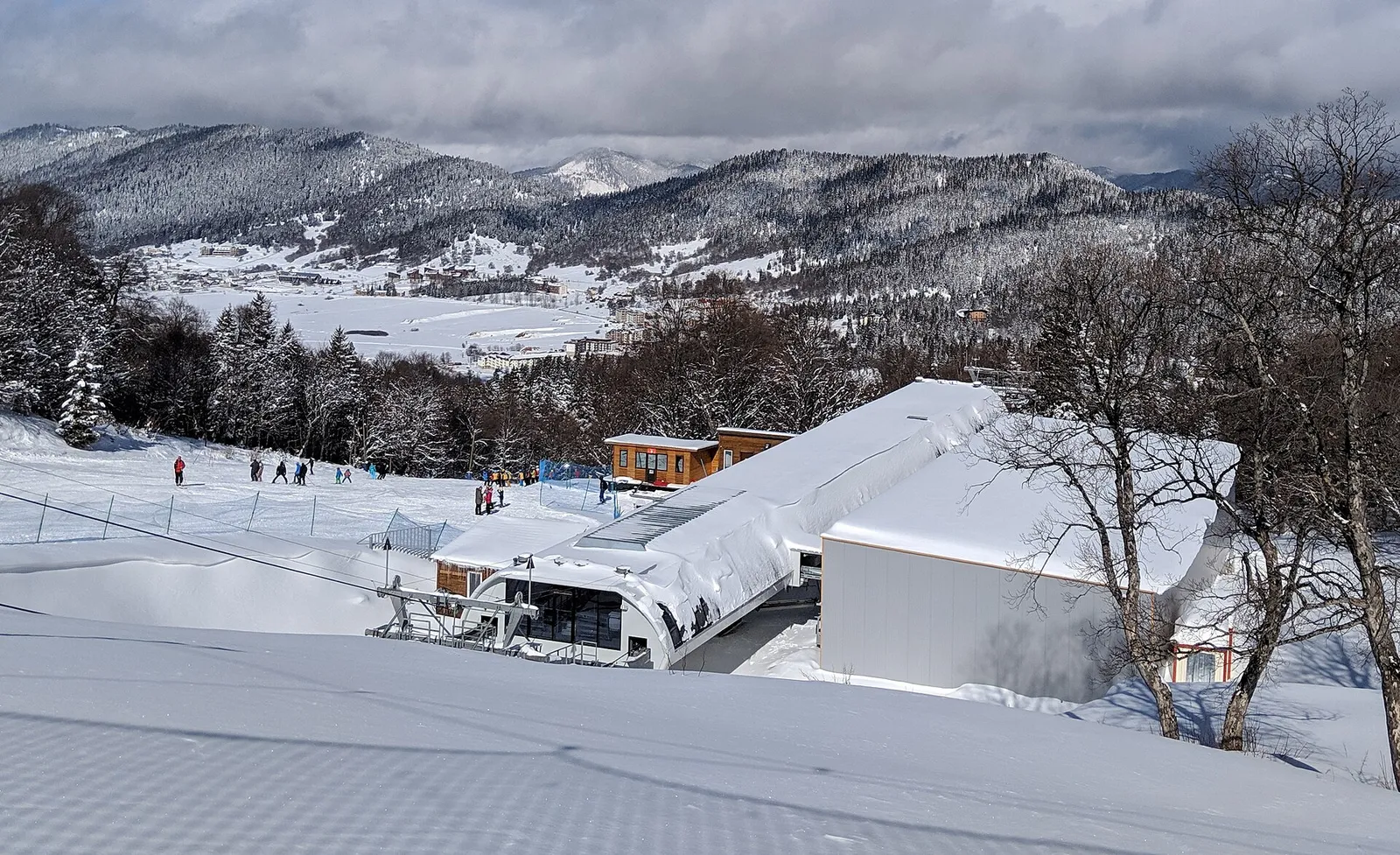 Chalets and skiers on the snow at a Georgian ski resort with wooded hills behind