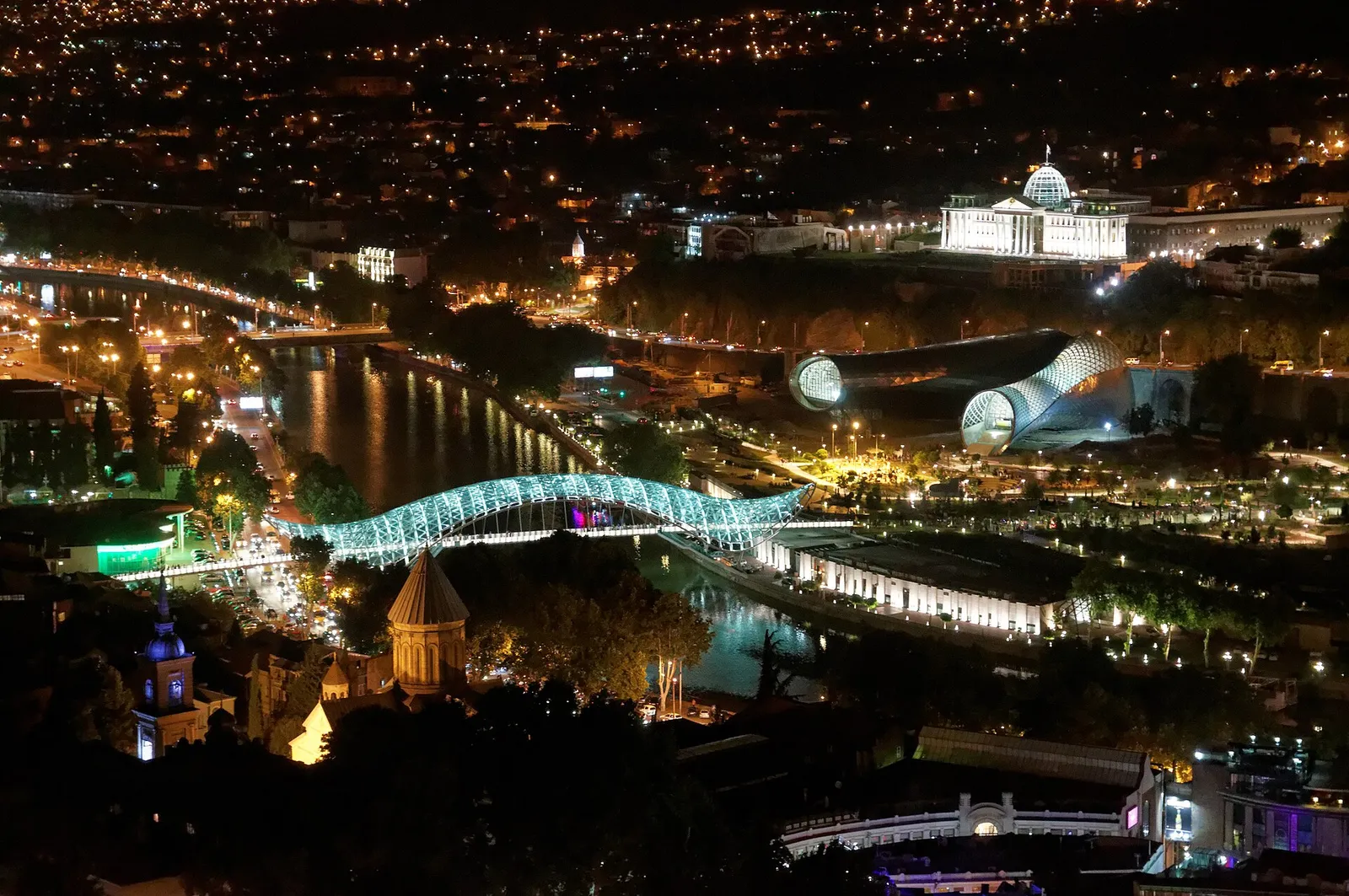 Aerial night view of Tbilisi with an illuminated bridge over the Kura river, Georgia