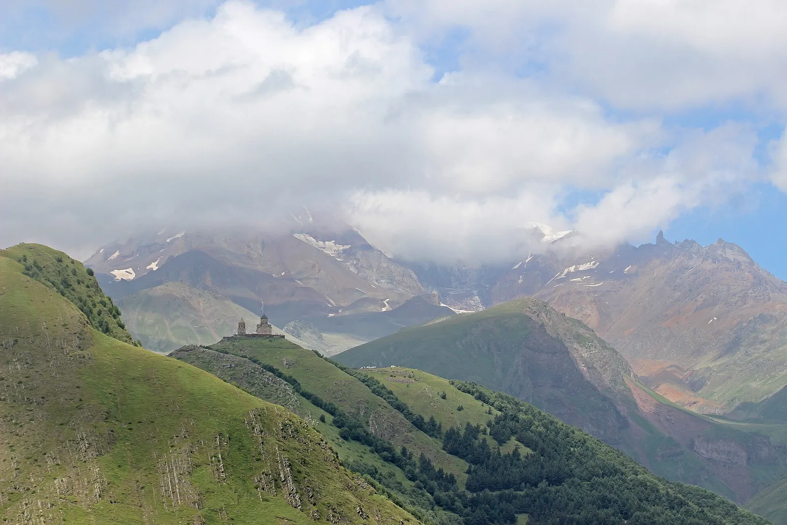 Green hills below high mountains with a small church on a ridge near Stepantsminda, Georgia