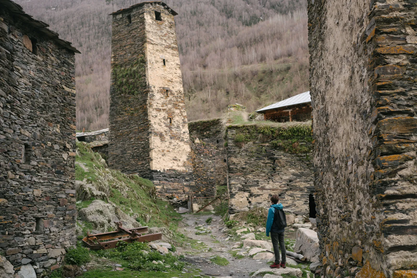 A walker looking up at an abandoned stone tower and slate roofed houses in a Caucasus mountain village