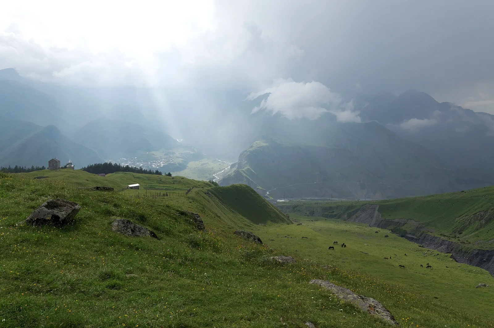 Green high pasture below the Kazbek range with cloud and low sun over the valley in Georgia