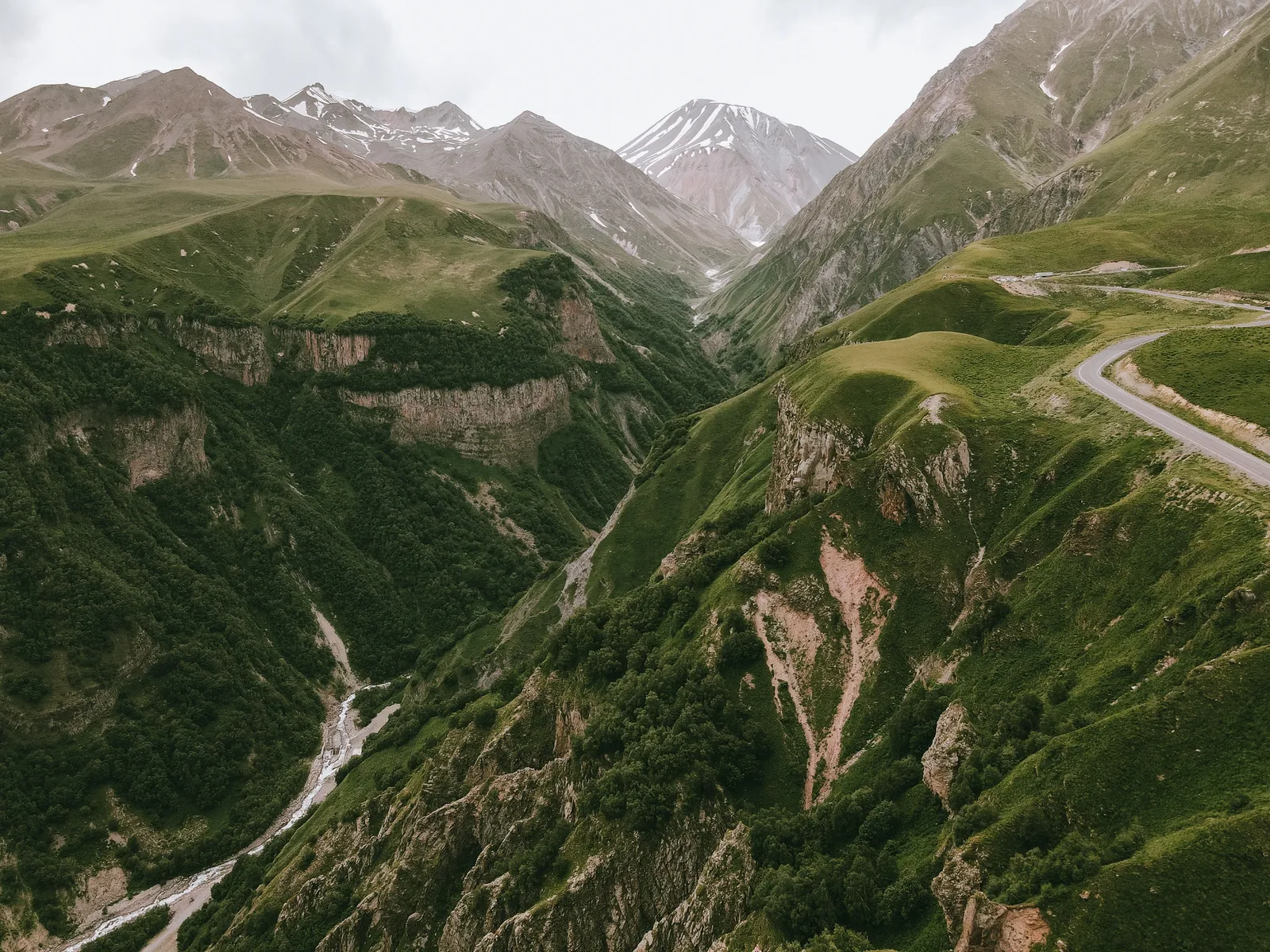 A deep green mountain valley in the high Caucasus of Georgia, with snow capped peaks on the horizon