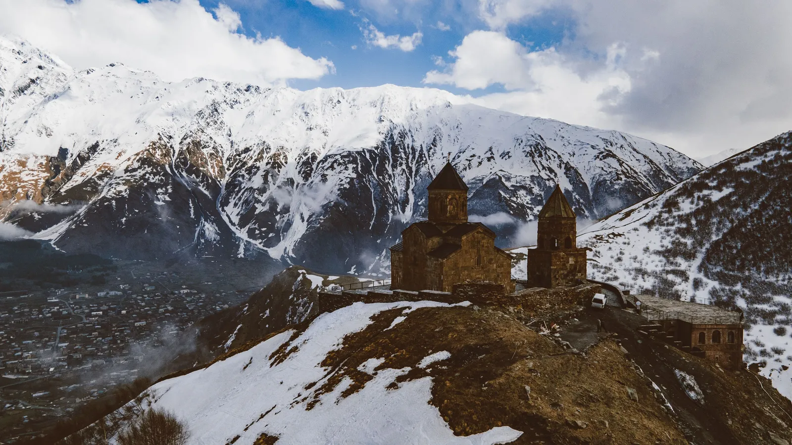 Church on a ridge with a snow covered mountain peak behind it in Kazbegi